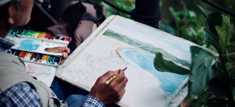 man holding paintbrush and paints, painting a landscape {{brizy_dc_image_alt entityId=